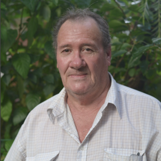 Warren standing in front of the garden he looks after. He has dark hair and is wearing a white shirt.
